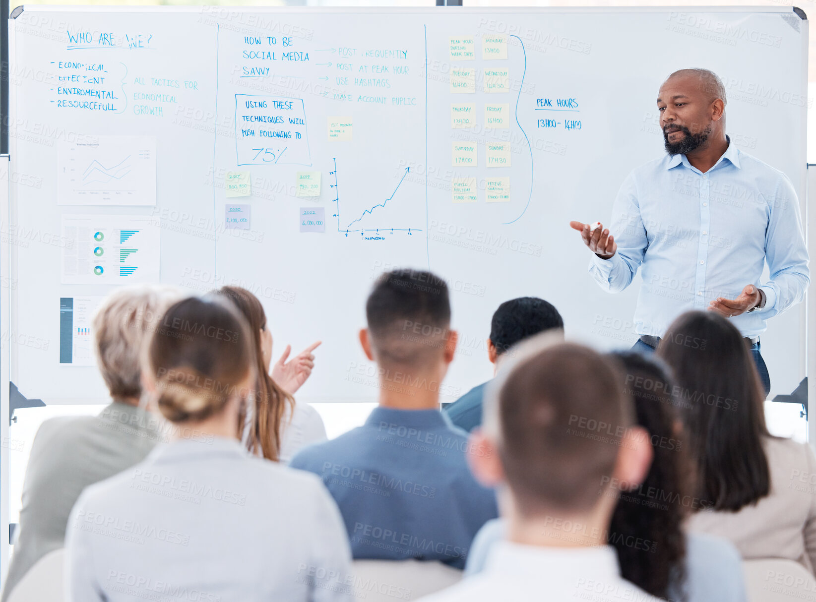 Buy stock photo Mature african american business manager training and teaching team of colleagues in office. Black businessman using a whiteboard to talk and explain to diverse group of business people in workshop