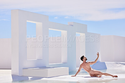 One handsome nude caucasian man posing naked like a greek god while lying outside by a pool of water. Sexy young male model looking sensual, sexy and seductive while flaunting muscular body in nude