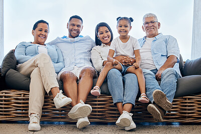 Portrait of extended hispanic family smiling at the camera while sitting on comfy couch. Adorable little girl bonding with her parents and grandparents. Multi-generation family sitting together