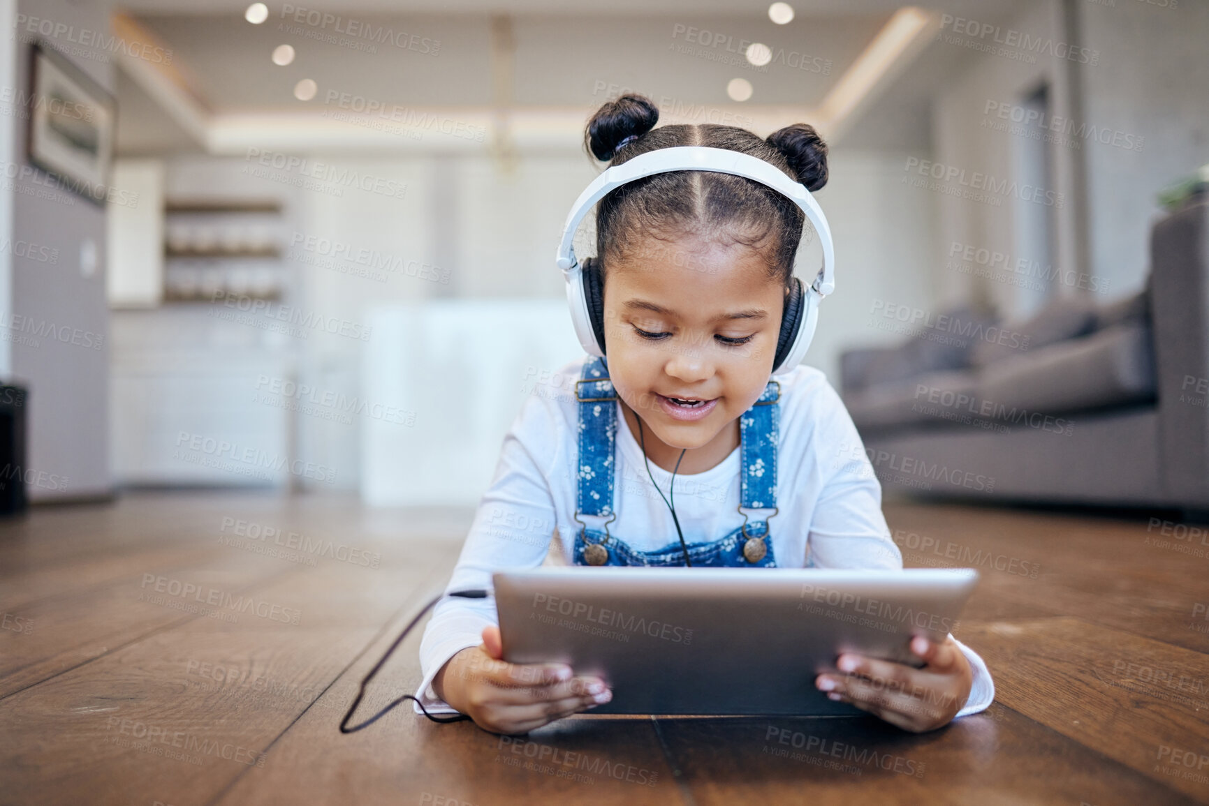 Buy stock photo Kid, headphone and tablet for streaming in home with internet for entertainment, learning or watching. Little girl, lying and floor in living room for comfort with technology for online, web or app