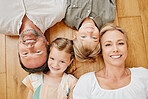 Top view of happy caucasian family lying together on the wooden floor at home. Portrait of a mature couple bonding with their two children at home. Adorable little girl and boy lying with mom and dad