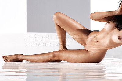 Cropped view of one unrecognizable sexy mixed race woman lying in a shallow pool of water in the nude on a sunny day. Naked unknown female model relaxing and posing outdoors