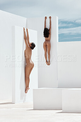 Two mixed race women modelling naked while climbing and hanging with their bodies pressed up a white wall outside. Sexy females looking sensual, erotic and seductive while flaunting their slim figures