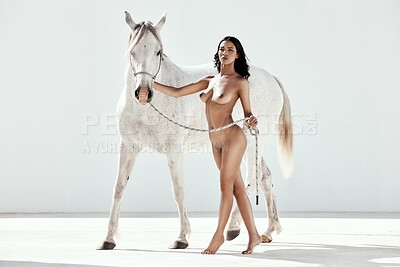 Full Body portrait of a beautiful mixed race woman posing nude while standing with white horse outside. Alluring hispanic model showing her naked body. Nudist feeling sensual, seductive and free