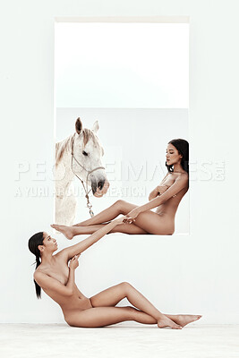 Two beautiful mixed race women posing nude while sitting with a horse outside. Sexy hot hispanic models showing her naked body and white stallion or mare. Nudist feeling sensual, seductive and free
