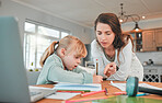Adorable little caucasian girl sitting at table and doing homework while her mother helps her. Beautiful serious young woman pointing and teaching her daughter at home. Parent home schooling her child