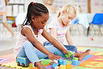 Little african american girl and classmate playing with colourful educational toy blocks on the floor at preschool or kindergarten. Kids having fun while engaged in creative learning and development