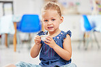 Portrat of one adorable little caucasian girl sitting alone in preschool and holding a small teacup. Smiling child playing and having a tea party at school. Social skills develop children at creche