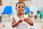 Portrait of one adorable little african american cute girl sitting alone in preschool and holding a small teacup. Smiling adorable child playing and having a tea party at school. Social skills develop children at creche