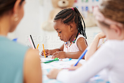 African american girl sitting at a table and colouring at pre-school or kindergarten with her fellow students. Young female child using colourful pencils to draw pictures in a classroom at her school