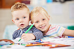 A portrait of two caucasian siblings sitting together at a table while being creative and drawing in a notebook. Smiling sister and brother bonding at homeschool. Blonde kids smiling while learning 