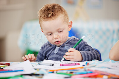 One cute little caucasian boy drawing a picture in a book while sitting alone at table and colouring at pre-school or kindergarten. Young child using colourful pencils to draw pictures in a classroom