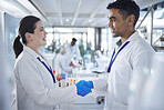 Two diverse professional scientist shaking hands while wearing blue gloves and lab coats. Two doctors making an agreement and congratulating one another. Hand gesture greeting of two people merging 