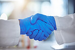 Cropped closeup of two unknown professional scientist shaking hands while wearing blue gloves and lab coats. Two doctors making an agreement and congratulating one another. Hand gesture greeting of two people