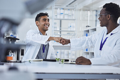 Two diverse mixed race professional scientist fist bumping and smiling while wearing lab coats. Two doctors making an agreement and congratulating one another. Hand gesture greeting of two people
