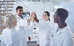 Diverse group of happy scientists giving each other a high give to celebrate their success while standing in a lab at work. Team of united workers smiling while joining their hands at work