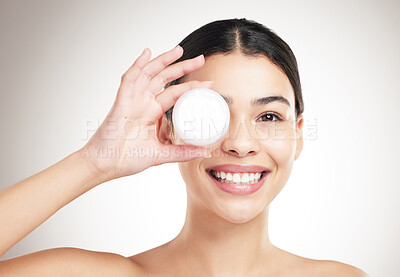 Buy stock photo Portrait of a young happy mixed race woman holding a lotion jar while standing against a grey studio background alone. One hispanic female applying cream to her body while standing against a background