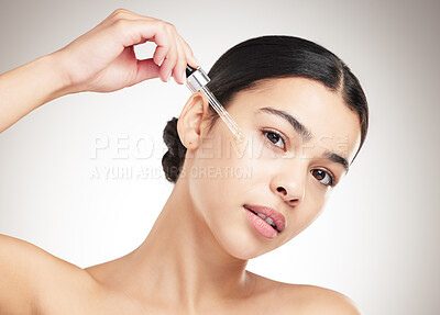 Buy stock photo Portrait of a young mixed race woman applying serum to her face while standing against a grey studio background alone. One hispanic female doing her skincare routine while standing against a background