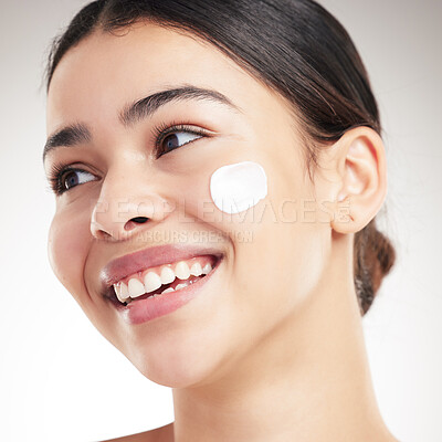 Buy stock photo Young joyful mixed race woman applying lotion to her face while standing against a grey studio background alone. One cheerful hispanic female doing her skincare routine while standing against a background