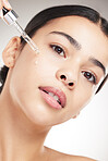 Portrait of a young beautiful mixed race woman applying oil to her face while standing against a grey studio background alone. One hispanic female doing her skincare routine while standing against a background