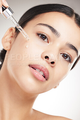 Buy stock photo Portrait of a young beautiful mixed race woman applying oil to her face while standing against a grey studio background alone. One hispanic female doing her skincare routine while standing against a background