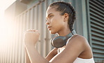 One fit young hispanic woman wearing headphones and doing squat exercises while training in an urban setting outdoors. Focused female athlete doing bodyweight warmup stretches to build muscle, strengthen body and increase endurance for workout