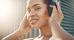 Closeup portrait of one fit young hispanic woman listening to music with headphones while exercising in an urban setting outdoors. Face of happy and motivated female athlete ready for training workout or run