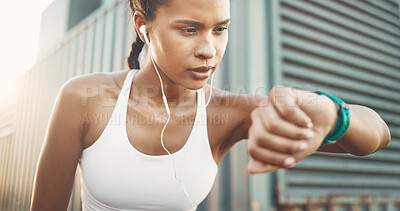 One active young hispanic woman wearing earphones and checking digital smartwatch while exercising in an urban setting outdoors. Female athlete wearing fitness tracker with stopwatch to monitor progress, heart rate and calories burned while training