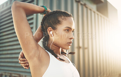 One fit young hispanic woman stretching arms for warmup to prevent injury while exercising in an urban setting outdoors. Focused and motivated female athlete listening to music with earphones while preparing body and mind for training workout or run