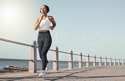 Buy stock photo Fitness, woman run at beach and with headphones listening to radio with lens flare. Training or exercise, marathon or sportswear and female person running along the promenade listen to music