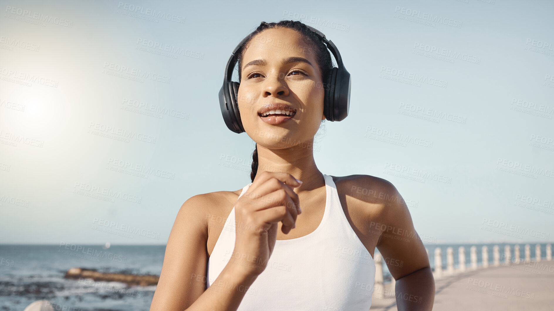 Buy stock photo Fitness, woman and running at seaside with headphones for exercise with wellness, audio and sunshine. Girl, listening and music with workout at ocean in summer for cardio or healthy body in morning.