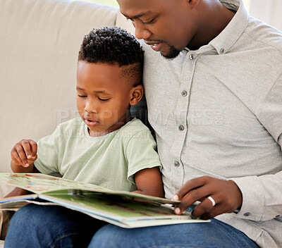 Young content African american father reading a book with his son sitting on the couch at home. Little boy enjoying a story and learning while sitting on the sofa with his dad on the weekend