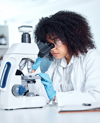 Buy stock photo One beautiful young african american woman with an afro wearing a labcoat and looking at medical samples on a microscope in her lab. A mixed race female scientist wearing goggles conducting research