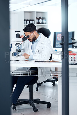 One mixed race scientist wearing safety goggles while analysing medical test samples with a microscope in a lab. Young indian man investigating with forensic research and experiments to develop a cure