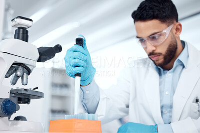 One mixed race male scientists wearing safety goggles and a labcoat while conducting medical research experiments with pipette and test tubes in a lab. Recording his findings for future investigation