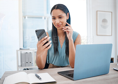 Happy young mixed race businesswoman smiling while using a phone and working on a laptop sitting in a chair in an office. One hispanic female boss using social media on a phone while sending an email