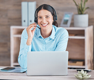 Portrait of a happy smiling hispanic woman wearing a headset and using a laptop while sitting at a desk at her office job. Cheerful young mixed race woman looking positive while working online