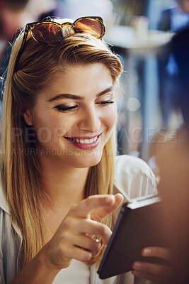 Beautiful caucasian woman smiling while using her smartphone in a cafe. Woman wearing sunglasses on her head and reading message or browsing social media while sitting
