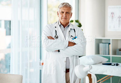 Buy stock photo Mature caucasian male expert doctor smiling while standing with his arms crossed working at a hospital alone. One senior man wearing a labcoat looking proud standing in an office at a clinic