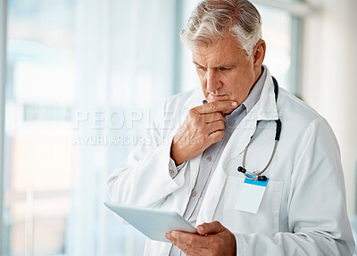 One mature male doctor thinking while browsing on a digital tablet device in a hospital or clinic. Senior caucasian man working with apps online to check medical records and research with telemedicine