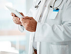 Closeup of expert male doctor holding and using a digital tablet, working at a hospital alone. One caucasian man wearing a labcoat working on a digital tablet standing in an office at a clinic