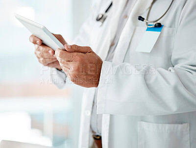 Closeup of expert male doctor holding and using a digital tablet, working at a hospital alone. One caucasian man wearing a labcoat working on a digital tablet standing in an office at a clinic
