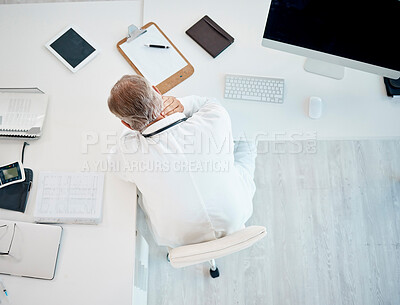 Buy stock photo Above view of tired and overworked male doctor rubbing his neck while sitting at his desk. Worried or upset senior physician feeling regret or guilt over medical malpractice while sitting alone