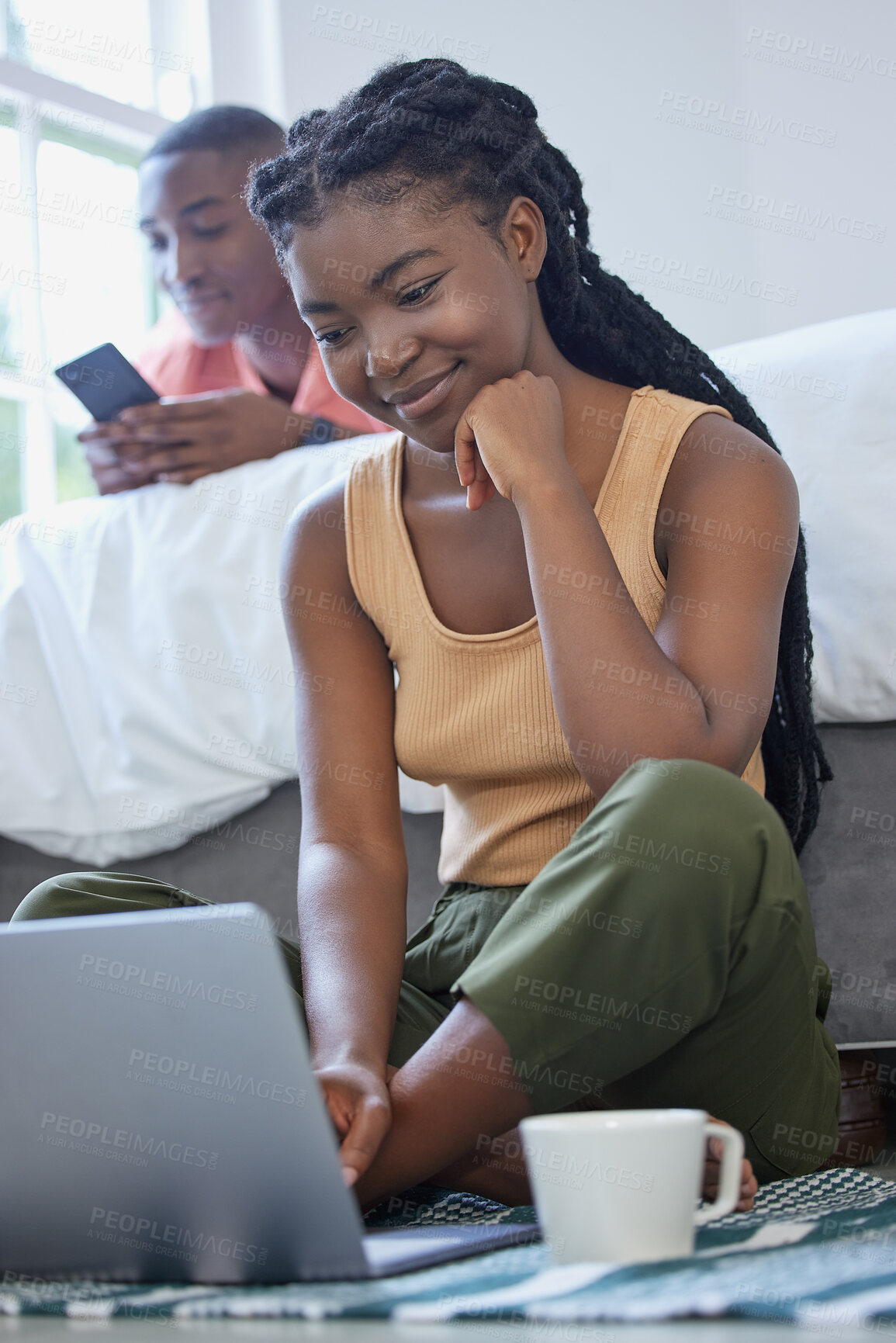 Buy stock photo Young african american man and woman sitting in the bedroom smiling and using wireless devices. Black couple using a laptop and phone on a weekend while enjoying coffee and quiet time at home