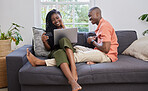 A young black african american couple smiling and laughing while using a laptop and credit card on a sofa at home. A affectionate black man and woman enjoying online shopping