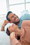 Happy young mixed race couple in a loving relationship laughing while relaxing together in bed at home. Boyfriend making a silly face while telling funny and lighthearted jokes to cheerful girlfriend