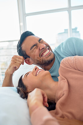 Buy stock photo Happy young mixed race couple in a loving relationship laughing while relaxing together in bed at home. Boyfriend making a silly face while telling funny and lighthearted jokes to cheerful girlfriend