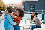Happy interracial couple hugging while spending time together outside at a restaurant with friends. African american man and mixed race woman embracing while having fun on the weekend
