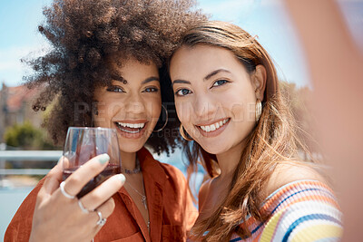 Buy stock photo Two beautiful young mixed race women standing together and taking a selfie while bonding outside. African american with an afro drinking wine with her asian friend. Capturing memories for social media