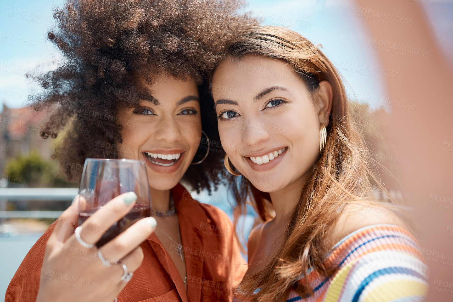 Buy stock photo Two beautiful young mixed race women standing together and taking a selfie while bonding outside. African american with an afro drinking wine with her asian friend. Capturing memories for social media